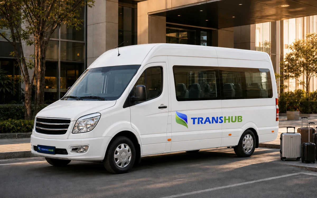 Illustrative white TransHub-branded group minibus outside a business hotel